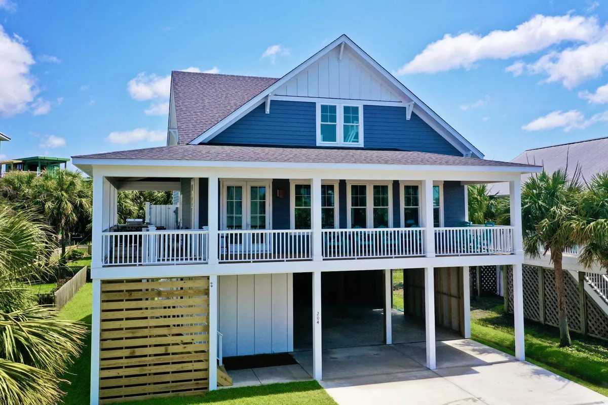 The image showcases the bright blue and white exterior of a spacious single-family house, framed by tropical palm trees. A large, inviting front porch offers comfortable seating and space to relax, with sunset lighting casting a warm, welcoming glow. The scene evokes a sense of relaxation and togetherness, ideal for gatherings or unwinding after a day at the beach.