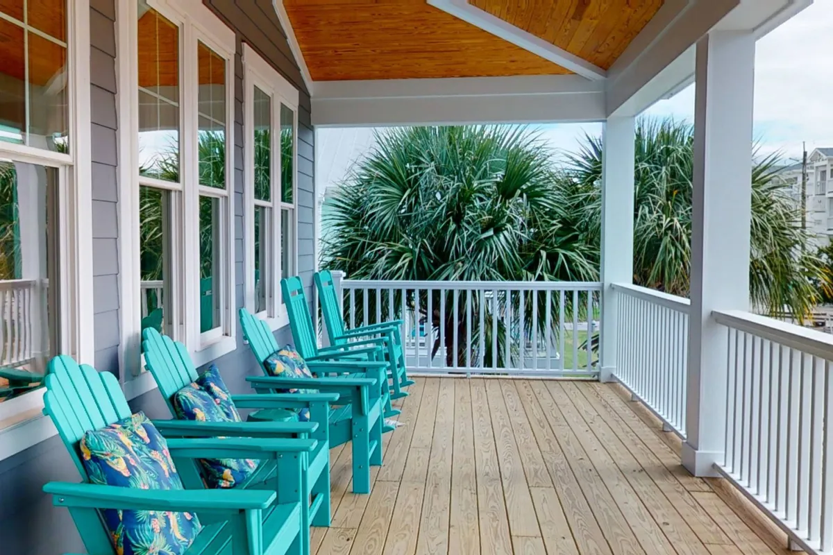 This image showcases a welcoming covered porch with turquoise Adirondack chairs adorned with decorative pillows, surrounded by lush palm trees. The scene invites relaxation and socializing, hinting at the kind of outdoor comfort and upscale touches described in the section.