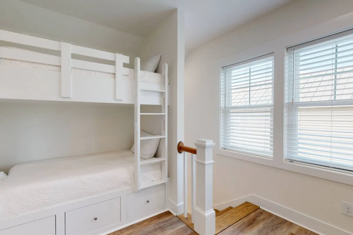 A light-filled loft area with a sturdy bunk bed, windows bringing in natural light, and a staircase railing. The inviting atmosphere combines coziness with functionality, ideal for both play and relaxation.