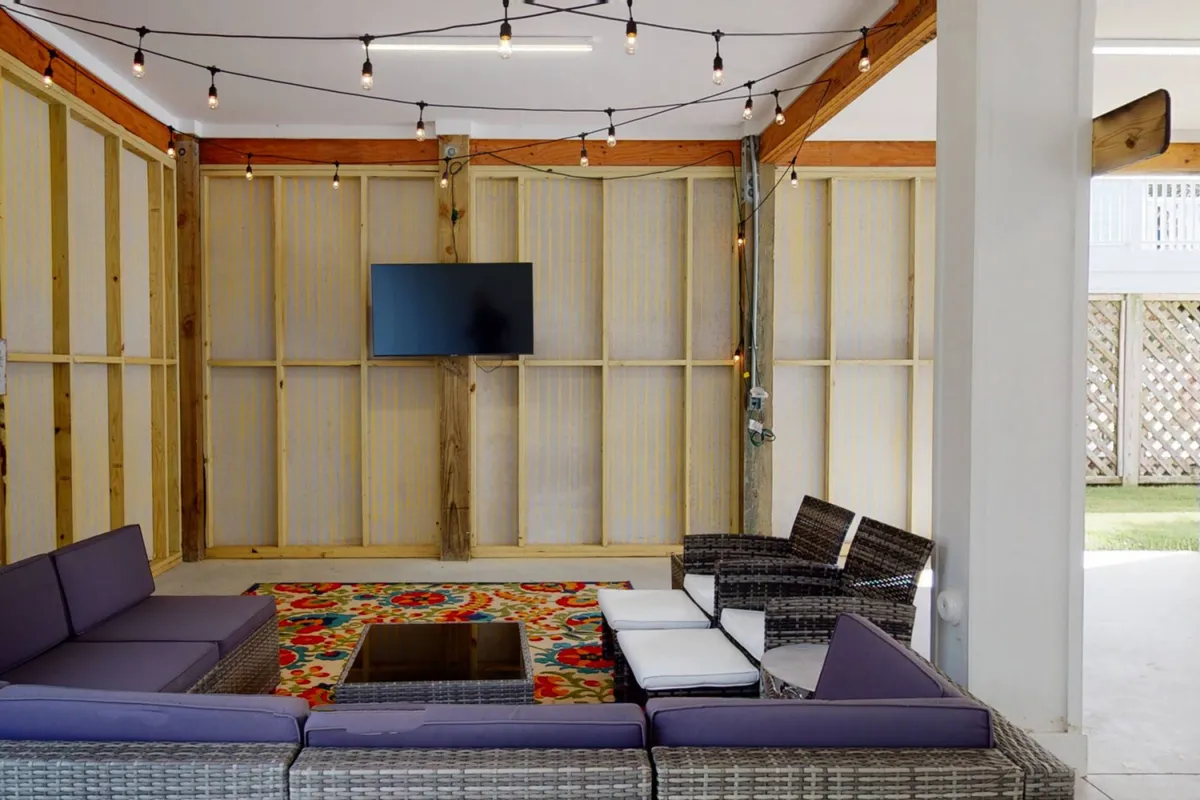 A large sectional sofa surrounds a colorful area rug, with a TV mounted on the wall and string lights overhead, creating an inviting space for movie nights and gatherings.