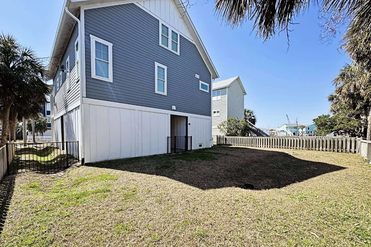 The exterior of Breezy Goin is featured, complete with a fully fenced yard surrounded by palm trees. The open space is ideal for both gatherings and play, making it safe for children and pets as described.
