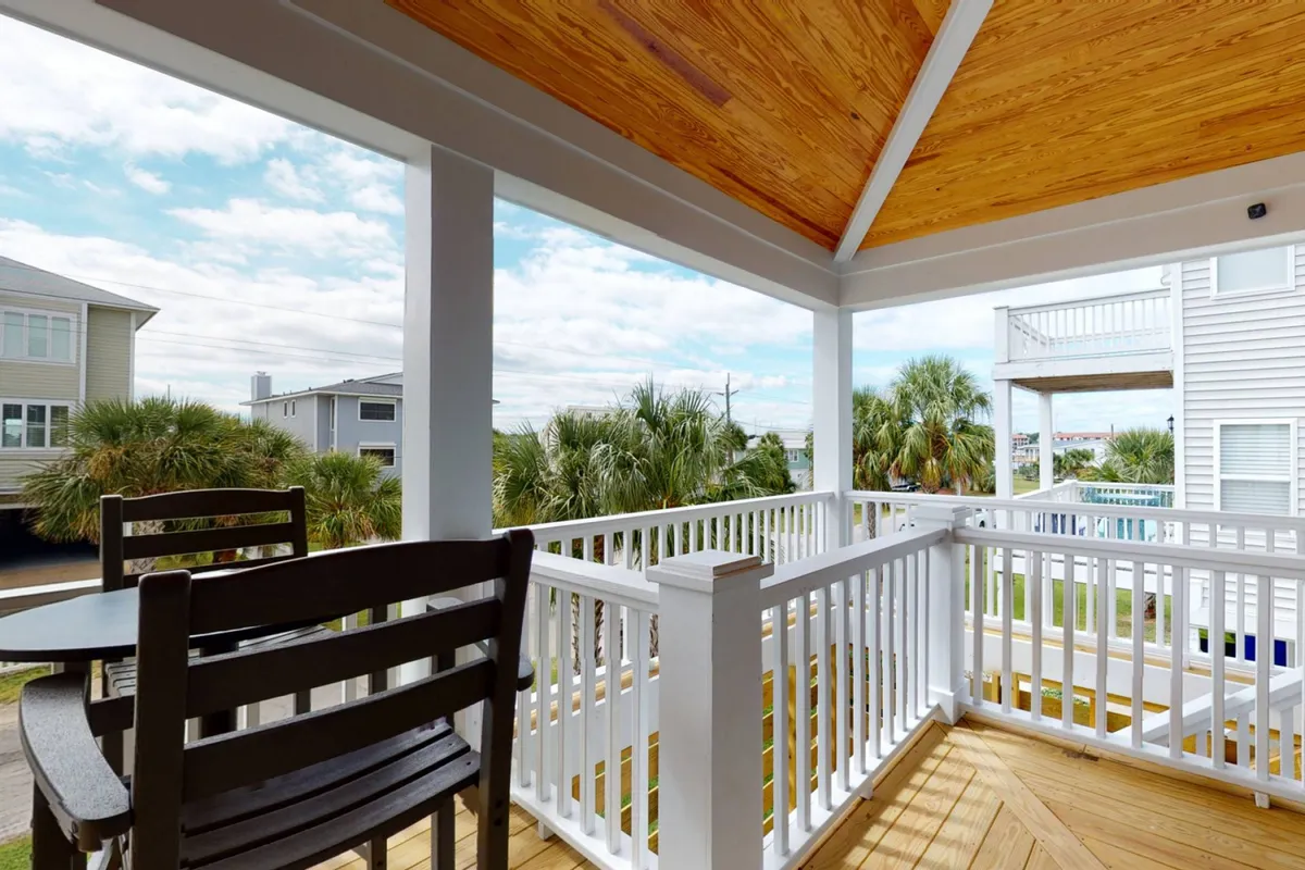 A tranquil wooden deck framed by lush palm trees, featuring a comfortable outdoor seating area ideal for relaxing, reading, or entertaining guests. The deck is covered, providing shade and shelter for gatherings at any time of day.