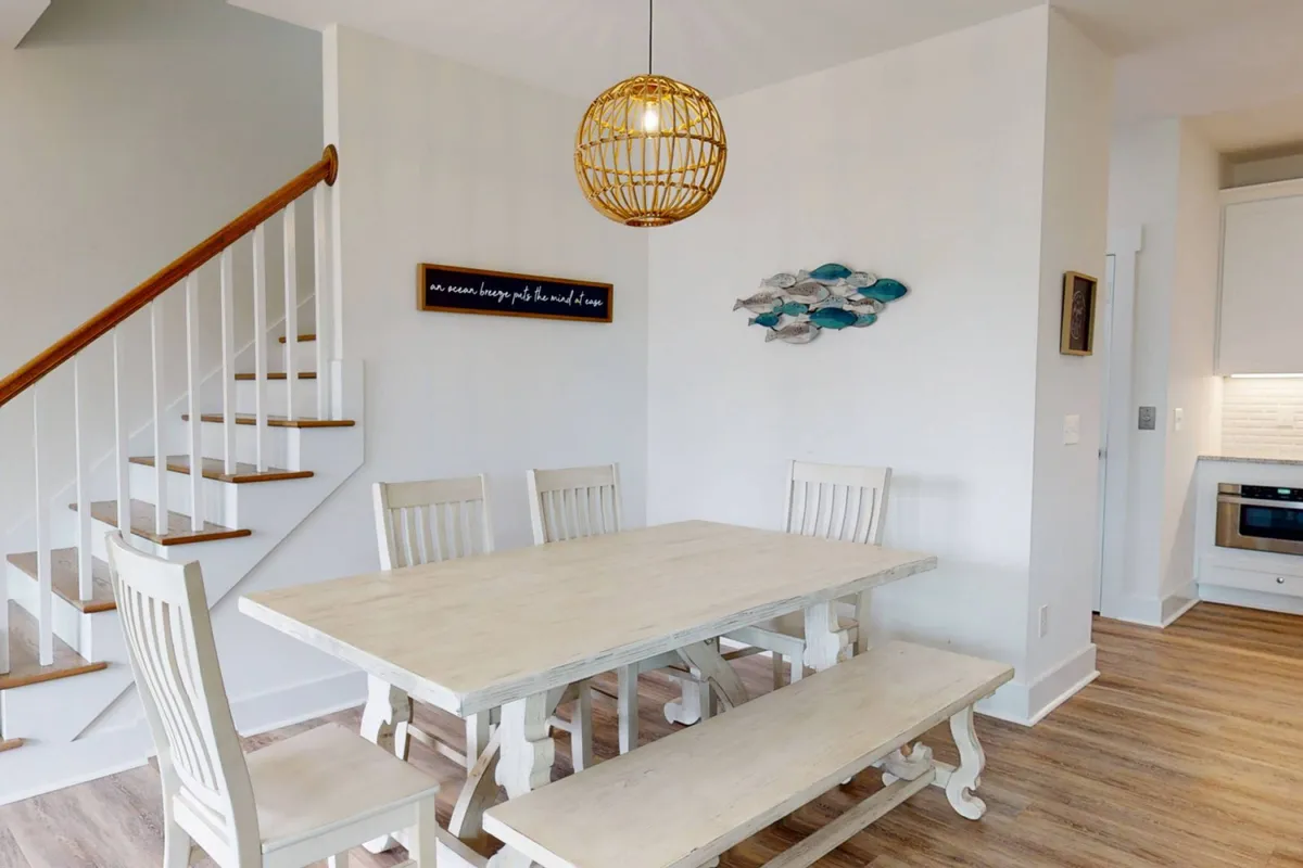 A welcoming dining area with a large table under a stylish light fixture, accented by coastal-themed fish wall art. The space is set for shared meals, celebrations, and heartfelt conversations.