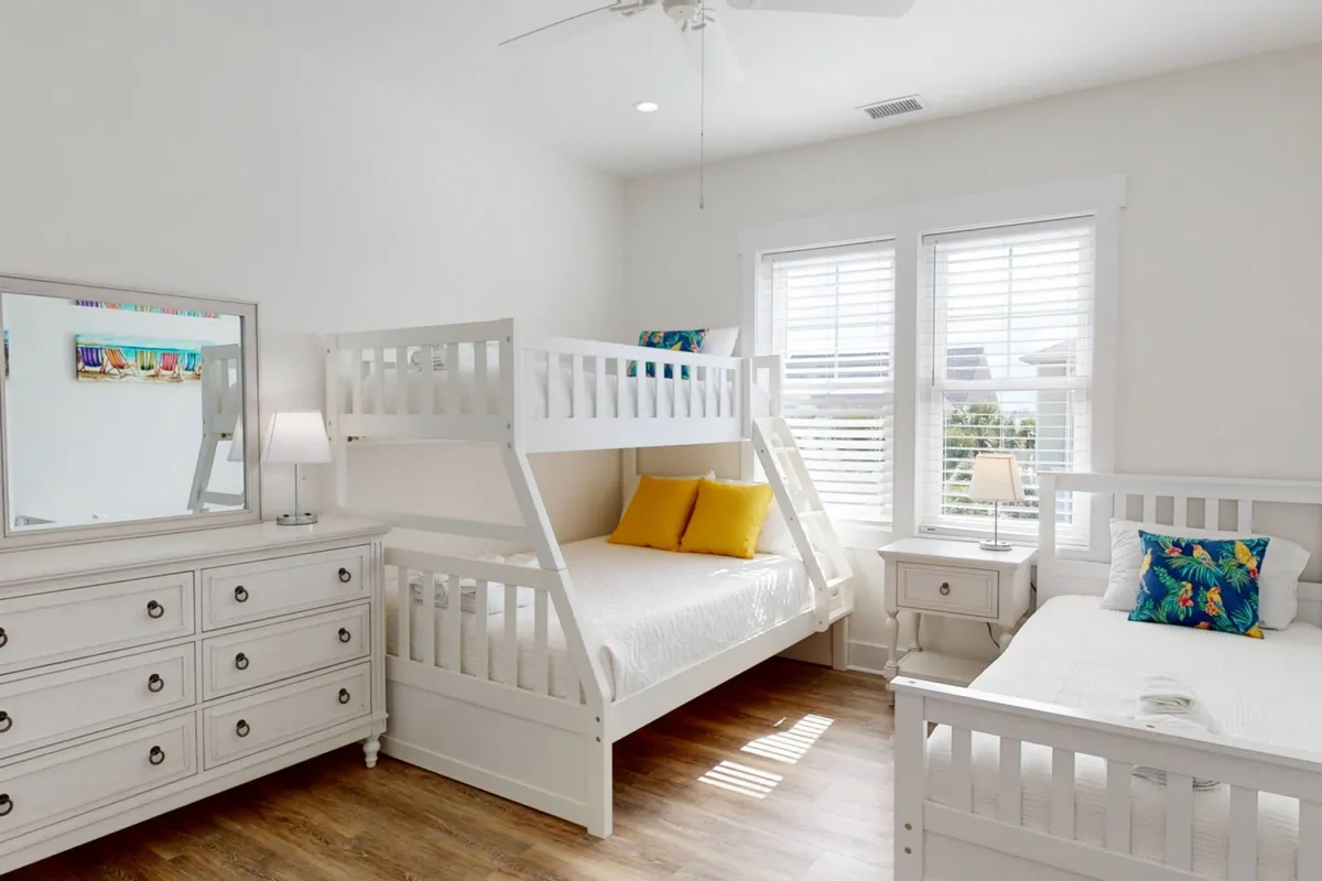 A playful and cozy bunk room featuring multiple bunk beds, a cheerful dresser, decorative pillows, and windows allowing natural light in. The vibrant setting is perfect for children or teens to play, read, and enjoy sleepovers.
